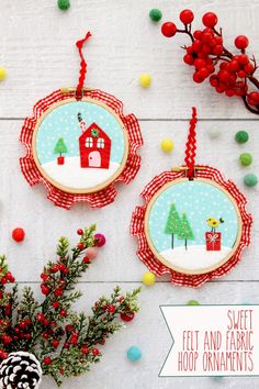 two christmas ornaments hanging on a white wall with decorations around them and small fir trees in the foreground