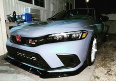 a silver car parked in front of a house with the hood up and lights on