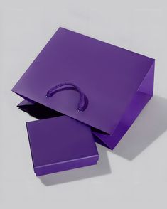 two purple bags sitting next to each other on top of a white surface with one bag in the middle