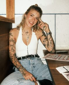 a woman sitting at a desk with tattoos on her arms and legs, talking on the phone