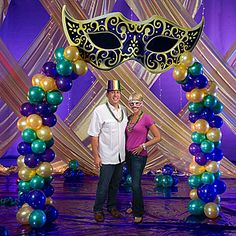 two people standing in front of a mardi gras arch decorated with beads and balloons