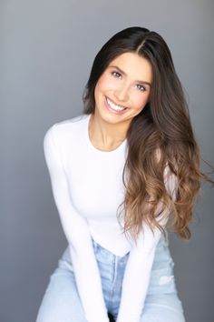 a woman with long brown hair and white shirt posing for a headshot in front of a gray background