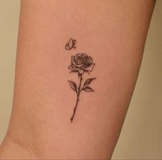 a small rose tattoo on the side of a woman's leg, with a butterfly flying over it