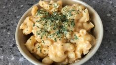 a white bowl filled with macaroni and cheese covered in parsley on top of a table