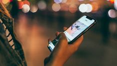 a person holding a cell phone in their hand and looking at the screen with blurry lights behind them