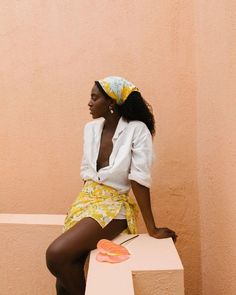 a woman sitting on top of a bench wearing a white shirt and yellow floral skirt