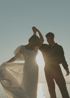 a man and woman standing next to each other in front of the ocean at sunset