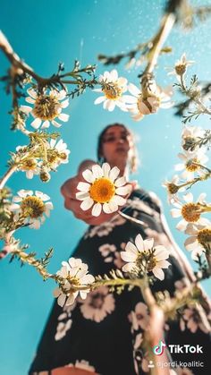 a woman holding a flower in her hand and looking up at the sky from below