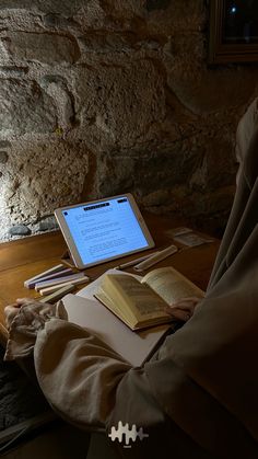 a person sitting at a table with an open book in front of their lap top