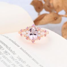 an oval shaped pink and white diamond ring on top of a book with leaves in the background