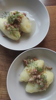 two white bowls filled with food on top of a wooden table