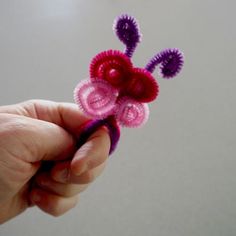 a hand holding a small crocheted flower with purple and pink petals on it