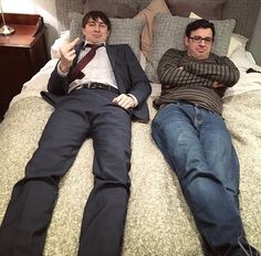 two men laying on top of a bed next to each other with their arms crossed