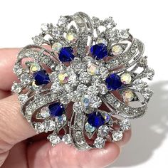 "Something blue bridal brooch with sapphire blue accent featuring flower or floral round shape made of sparkly clear mixed with AB iridescent colored rhinestone crystals in tarnish-resistant silver rhodium plated base.   Brooch measures about 2 1/8\" (5.5cm) in diameter. Note: AB (Aurora Borealis) crystal has an iridescent coating that gives it a subtle shimmer which takes on the colors around it. * Limited, only a few left now View all something blue designs at https://etsy.me/1aLVWtA View all Crystal Flower Brooch For Weddings, Blue Brooch For Wedding Jewelry, Blue Wedding Brooch Jewelry, Wedding Brooches With Rhinestones, Blue Round Brooch For Formal Occasions, Blue Flower Brooch For Wedding, Formal Blue Round Brooch, Formal Blue Round Brooches, Elegant Blue Wedding Brooches