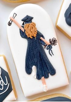 cookies decorated to look like women in graduation gowns and holding a stick with writing on them