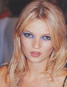 a woman with blue eyes and long blonde hair is posing for a photo in front of the camera