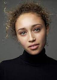 a woman with curly hair wearing a black turtle neck shirt and looking at the camera