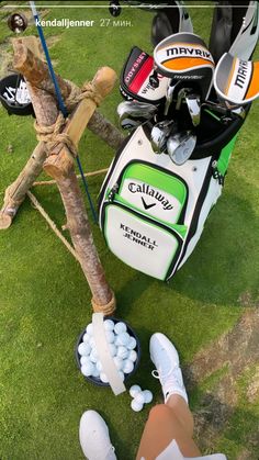 a golf bag, clubs and balls sitting on the grass next to a person's feet