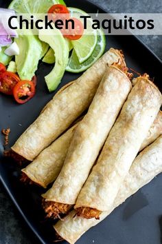 several burritos are on a black plate next to some vegetables and lime wedges