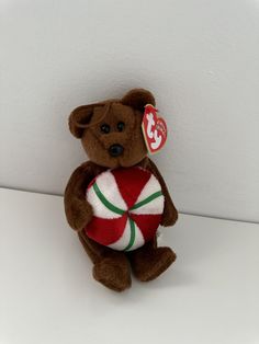 a brown teddy bear holding a red and white striped candy ornament on it's chest