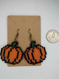 an orange and black beaded pumpkin earrings next to a dime coin on a card