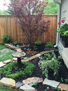 a small garden with rocks and flowers in the back yard, next to a wooden fence