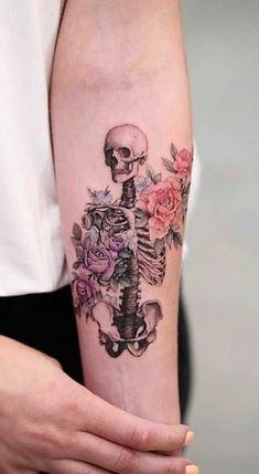 a person with a skull and roses tattoo on their arm, holding onto the arm