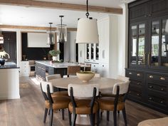 a dining room table and chairs in front of an open kitchen area with black cabinets