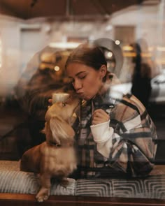 a woman sitting on a bench with her dog and drinking from a cup in front of her