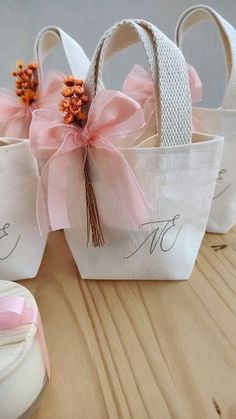 three small white bags with pink bows on them sitting on top of a wooden table