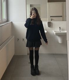 a woman standing in a bathroom taking a selfie with her cell phone while wearing knee high socks