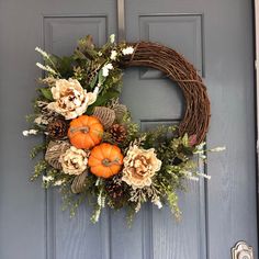 a wreath with flowers and pumpkins is hanging on the side of a blue door