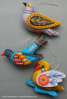 three colorful bird ornaments hanging from strings on a gray surface with text overlay that says, ` `