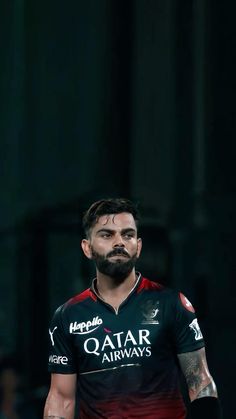 a man with tattoos on his arm wearing a black and red shirt, standing in front of a dark background