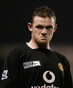 a man in a black shirt standing on a soccer field with his head turned to the side