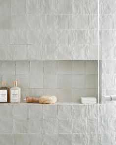 a white tiled bathroom with two bottles and soaps on the shelf next to it