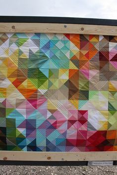 a multicolored quilt hanging from a wooden frame