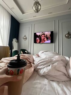 a coffee cup sitting on top of a bed next to a flat screen tv in a bedroom