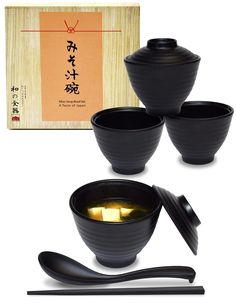 three black bowls with chopsticks in front of an orange box and two wooden spoons