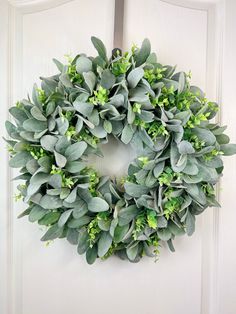 a wreath is hanging on the front door with green leaves and greenery around it