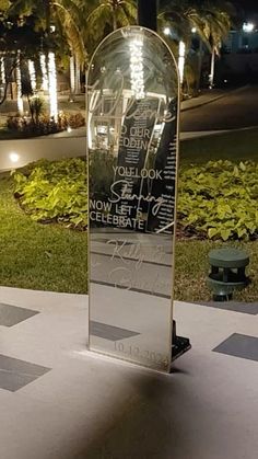 a glass sign sitting on top of a cement slab in the middle of a park