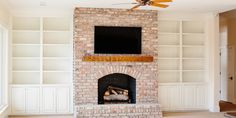 a living room with a brick fireplace and tv mounted on the wall, along with built in bookshelves