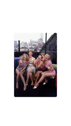 four women sitting on a bench in front of a city skyline