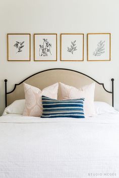 a bed with three framed pictures on the wall above it and two blue and white pillows