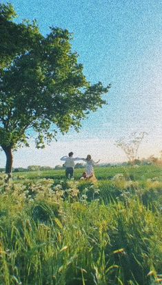 two people standing in the grass under a tree with their arms up to each other