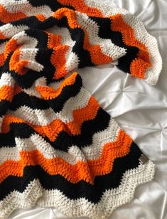 an orange and black crocheted blanket laying on top of a white bedspread