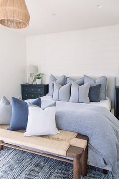 a bed with blue and white pillows on top of it in a bedroom next to a dresser