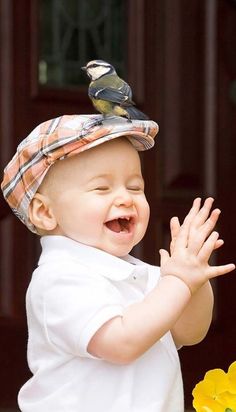 a little boy that is standing up with a bird on top of his head and hands in the air