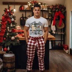 a man standing in front of a christmas tree wearing plaid pants and a t - shirt that says time for beer