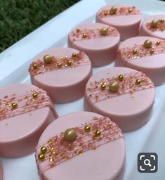 some pink and gold decorated cakes on a white platter with grass in the background